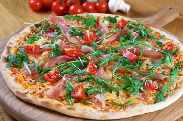 Pizza with prosciutto , arugula and parmesan on wooden background top view. Italian cuisine.
