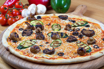 Tasty fresh pizza decorated with mushrooms and zucchini on wooden background