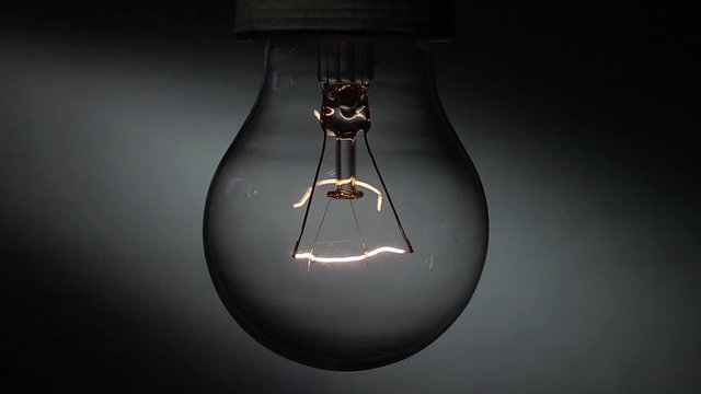 Una vecchia lampada al tungsteno in primo piano si accende e si spegne lentamente.