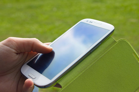 Smartphone tactile blanc dans une main, reflets de ciel et de soleil dans le téléphone avec fond de nature