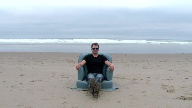 Man sitting on cozy armchair lifts hand and clicks an invisable remote control at the Oregon Coast.