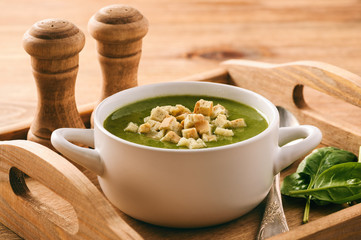 Green cream vegetable soup with croutons on wooden tray.