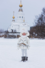 Fototapeta na wymiar cute little girl is going to the rink with skates in winter snowy day. in the background the church.