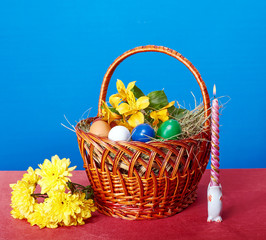 Easter basket with flowers and Easter eggs near a burning candle