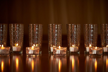 Many burning candles in transparent glasses, shiny floor, the reflection. Mood, relaxation, prayer and comfort