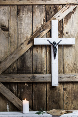 Wooden white cross, prayer, candle and olive branch on a background of the old wooden walls