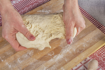 Hardworking female hands kneading dough on wooden kitchen table with love