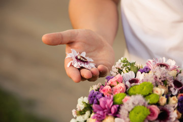 Proposal of marriage. Engagement ring on colorful flower on hand of man. Boy makes proposal with golden wedding ring 