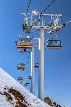 Skiers and snowboarders being transported on a chair ski lift in Sochi mountain ski resort on a sunny winter day on blue sky background. Vertical landscape