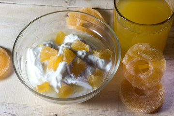 Breakfast with Yogurt with pieces of pineapple and orange juice on a wooden background