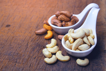 cashew nuts and roasted salt cashew nut in shell on white ceramic spoon.