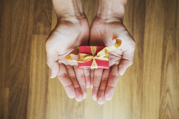 A man hand holding red gift box on hand, on wood background