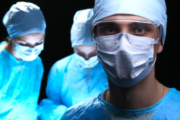 Three surgeons at work operating in surgical theater saving patient and looking at life monitor. Resuscitation medicine team wearing protective masks. Surgery and emergency concept