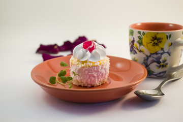 Small cake with cream, cherries and coconut topping on a ceramic plate