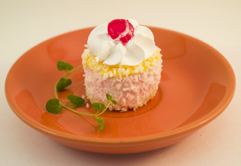 Small cake with cream, cherries and coconut topping on a ceramic plate
