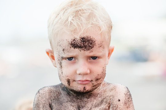 Funny photo of happy baby boy on beach with dirty face covered with black sand. Family travel, healthy lifestyle, recreation, water outdoor activity on summer beach vacation with children