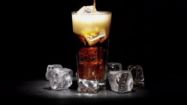 In glass with ice poured cola on a black background. 4K video.