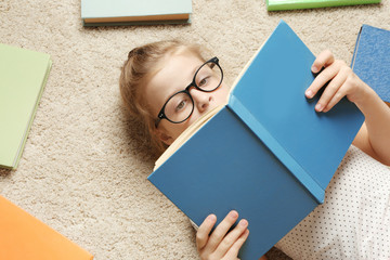 Cute little girl reading book while lying on carpet