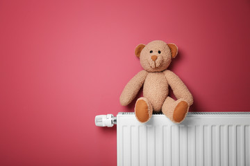 Fototapeta premium Teddy bear on heating radiator near pink wall