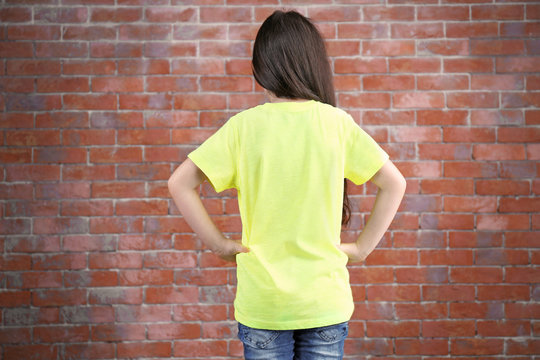 Little girl in blank color t-shirt standing against brick wall