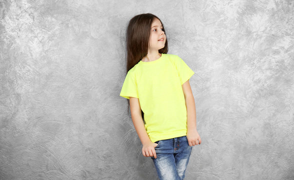 Little girl in blank color t-shirt standing against grey textured wall