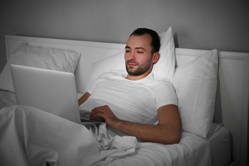 Young man with laptop lying in bed