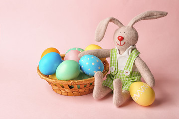 Basket with colorful Easter eggs and bunny on pink background