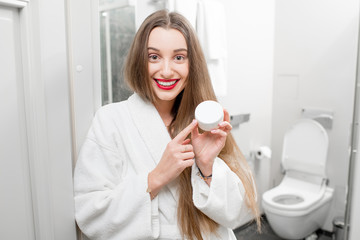 Happy woman holding bottle with cream in the bathroom