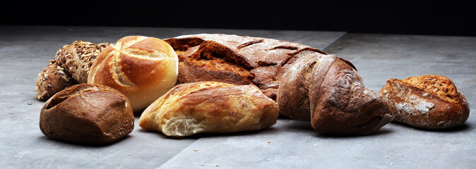 Different kinds of bread rolls on black board from above. Kitchen or bakery poster design.