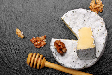 Camembert cheese with nuts and spoon for honey and honey on dark slate background.top view