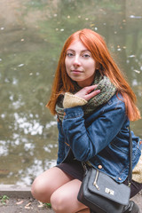 Red-haired girl with freckles sitting on a background of water and looking at the camera.