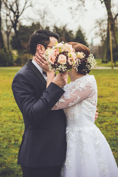 Hochzeit, Ehepaar verdeckt Kuss mit Brautstrau&szlig; vor den Gesichtern