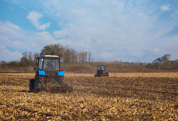 Obraz premium Two large blue tractor plow plowed land after harvesting the maize crop on a sunny clear autumn day.