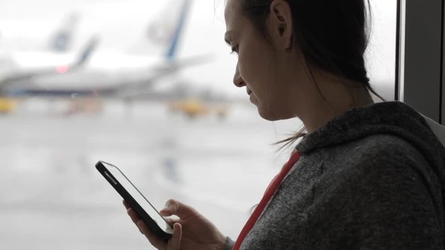 Young woman using smart phone at airport with airplane on the background
