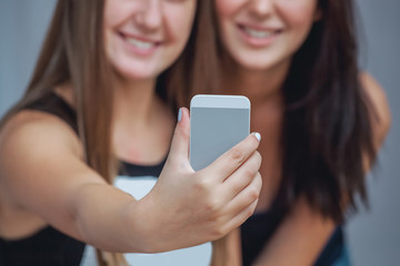 Two young attractive smiling woman holding a cell phone and make a selfie.