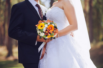 Bride and groom holding wedding bouquet together, outdoor. Love.