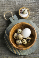 Obraz na płótnie Canvas Quail eggs in a wooden bowl on cutting board dark background with salt. Top view