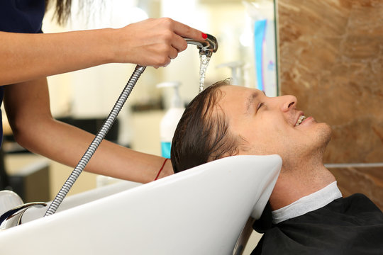 Female hands washing hair to handsome smiling man