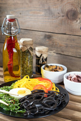 Hiyashi wakame with sesame and nut sauce, black and corn noodles, boiled egg. Octopus and mussels in ceramic bowls, bottle of olive oil with chili pepper, black olives and capers in jar, bran bread