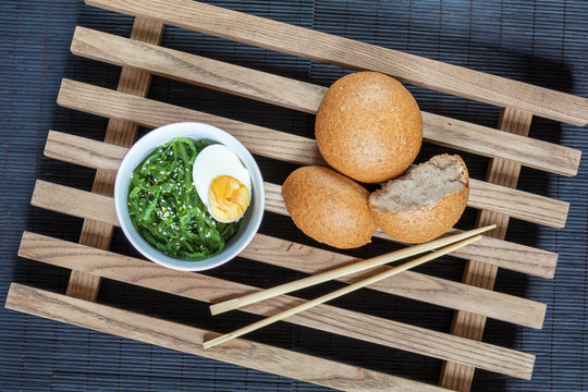 Hiyashi wakame with sesame and nut sauce, boiled egg in ceramic bowl and bran bread on the rustic wooden lattice and black makisu