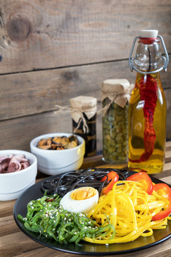 Hiyashi wakame with sesame and nut sauce, black and corn noodles, boiled egg. Octopus and mussels in ceramic bowls, bottle of olive oil with chili pepper, black olives and capers in jar, bran bread