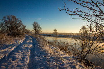 Winter landscape with snow, river, blue sky, road, sunshine, ice.