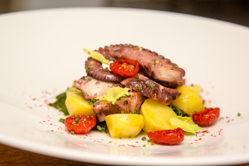 Potato salad with octopus and sun dried tomatoes lies on the pla