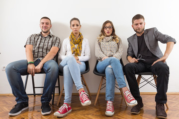 Group of young people is sitting in a row in an office lobby and waiting for the job interview.