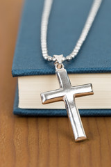 Necklace with silver cross on wooden table and blue bible book