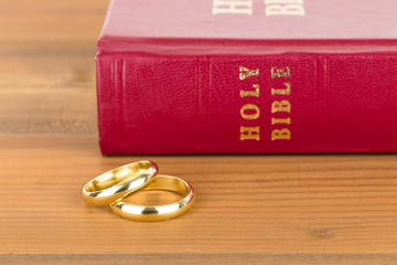 Gold wedding rings on wooden table and red bible book