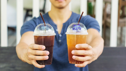 Man drinking an iced coffee and iced tea in a cafe.
