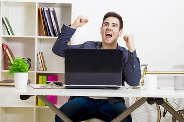 young man with arms raised with computer laptop enthusiastically celebrating success