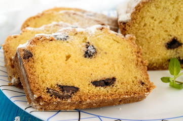 Freshly baked homemade cakes, decorating the top with powdered sugar, cut slices, with pieces of chocolate on a plate on blue background. Close up