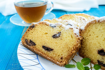 Freshly baked homemade cakes, decorating the top with powdered sugar, cut slices, with pieces of chocolate on a plate on blue background. Close up
